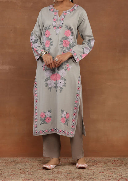 Woman wearing a light gray kurta with floral embroidery against a brown background