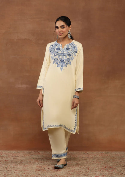 Woman wearing a cream kurta with blue embroidery against a brown background